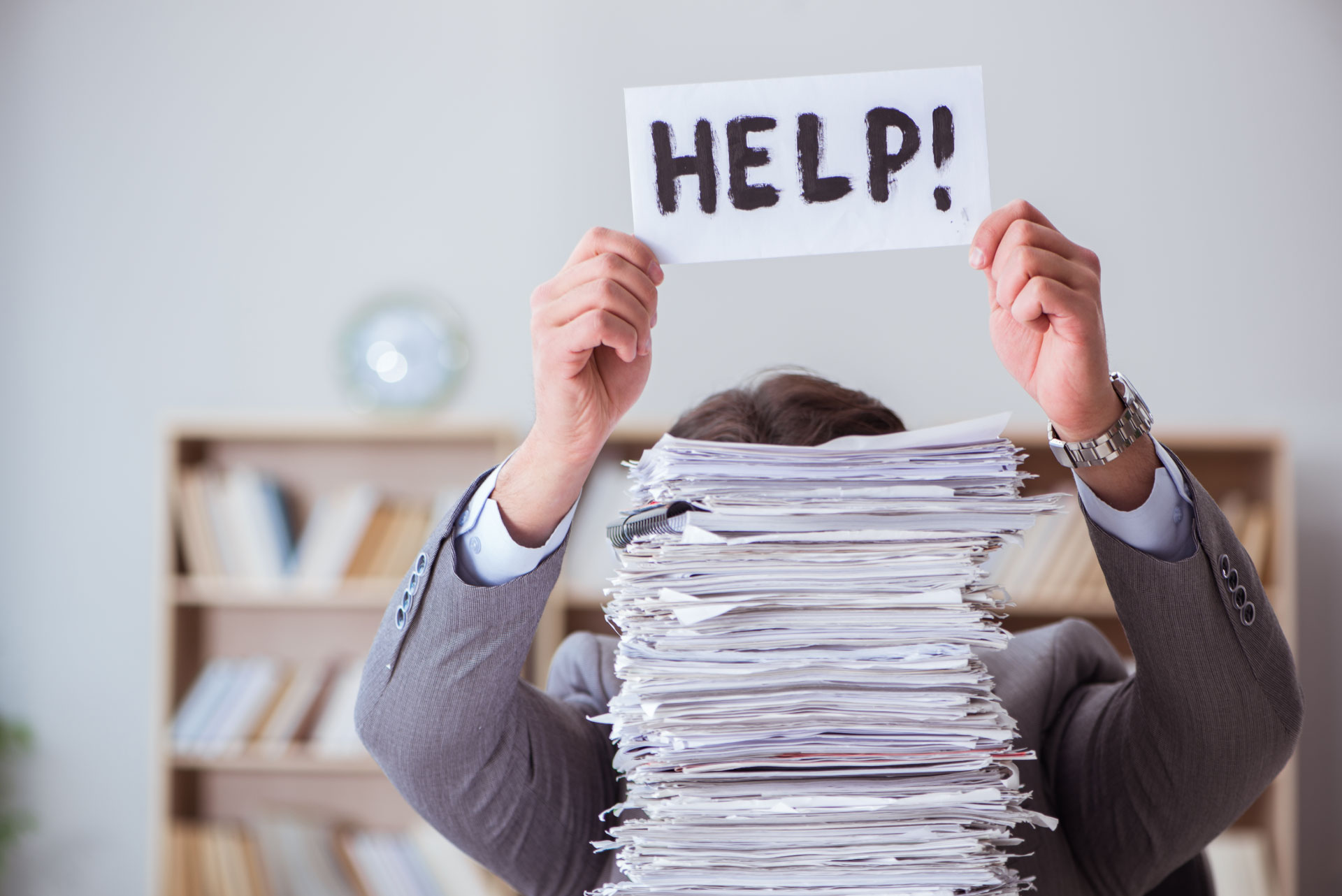 Image of a stack of office papers with a person behind holding a help sign